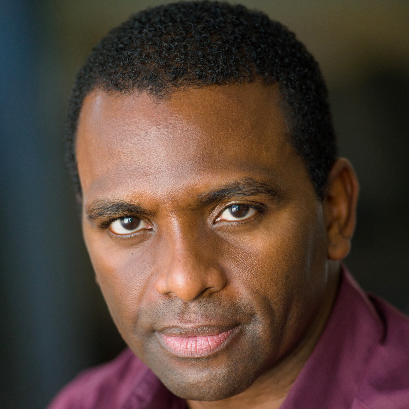 Professional headshot of a man in a burgundy collared shirt, looking directly at the camera with a confident and approachable expression.