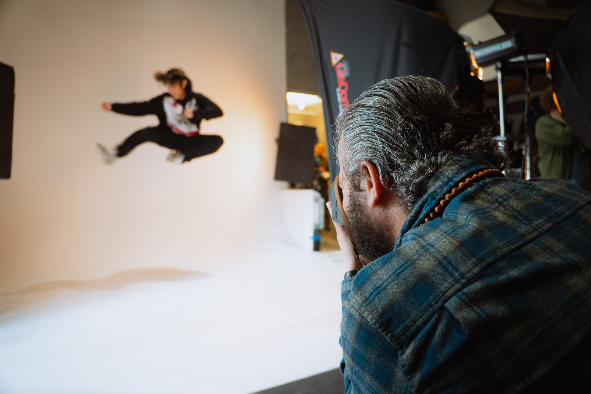 A photographer captures an action shot of a person performing a high jump kick in a photography studio with professional lighting equipment.