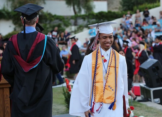 graduate student in white gown smiling walking off of the ceremony podium